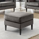 Gray ottoman in a living room setting with gray chairs and a white rug.