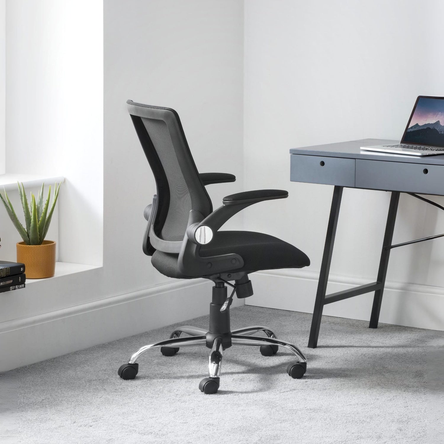 Black office chair in front of a desk with a laptop in a minimalistic room.