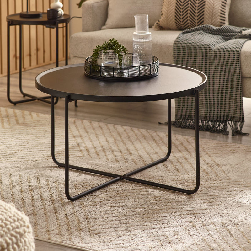 Round black coffee table in a living room setting with decor items on top.