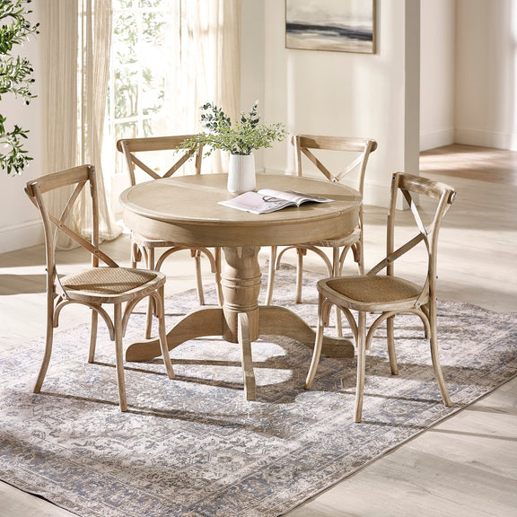 Round wooden dining table with four matching chairs in a bright room.