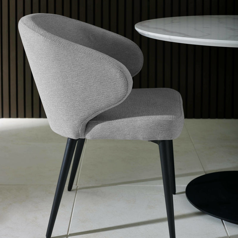 Gray upholstered chair with black legs in a room with a marble table and tiled floor.
