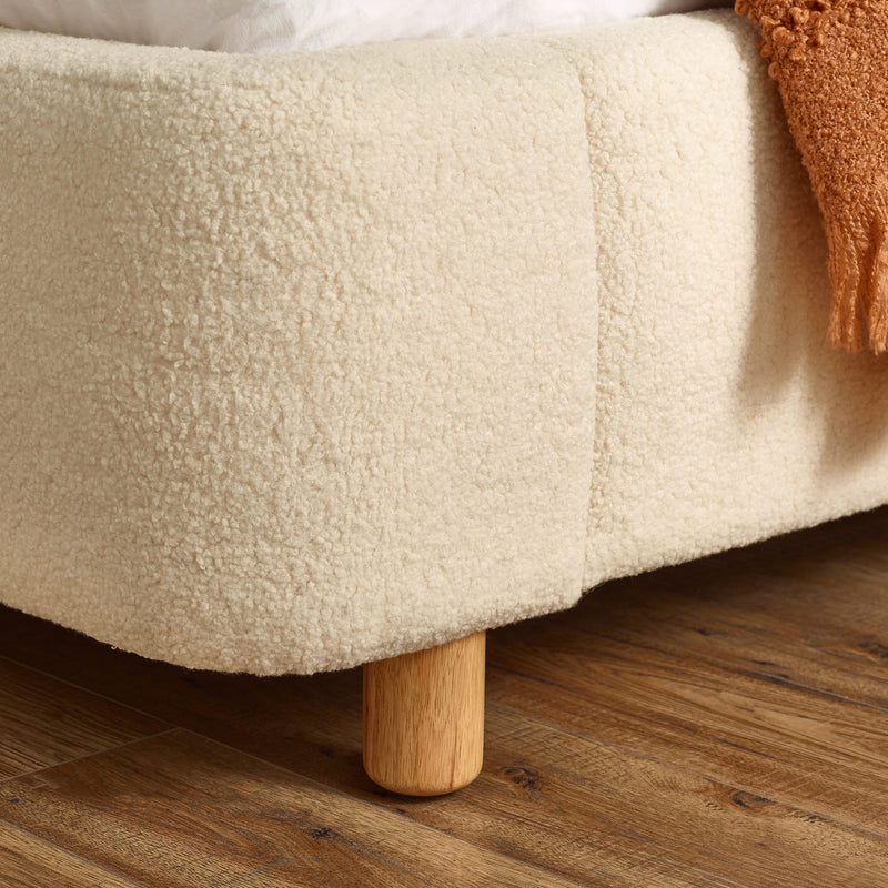 Beige textured ottoman with wooden legs on a wooden floor