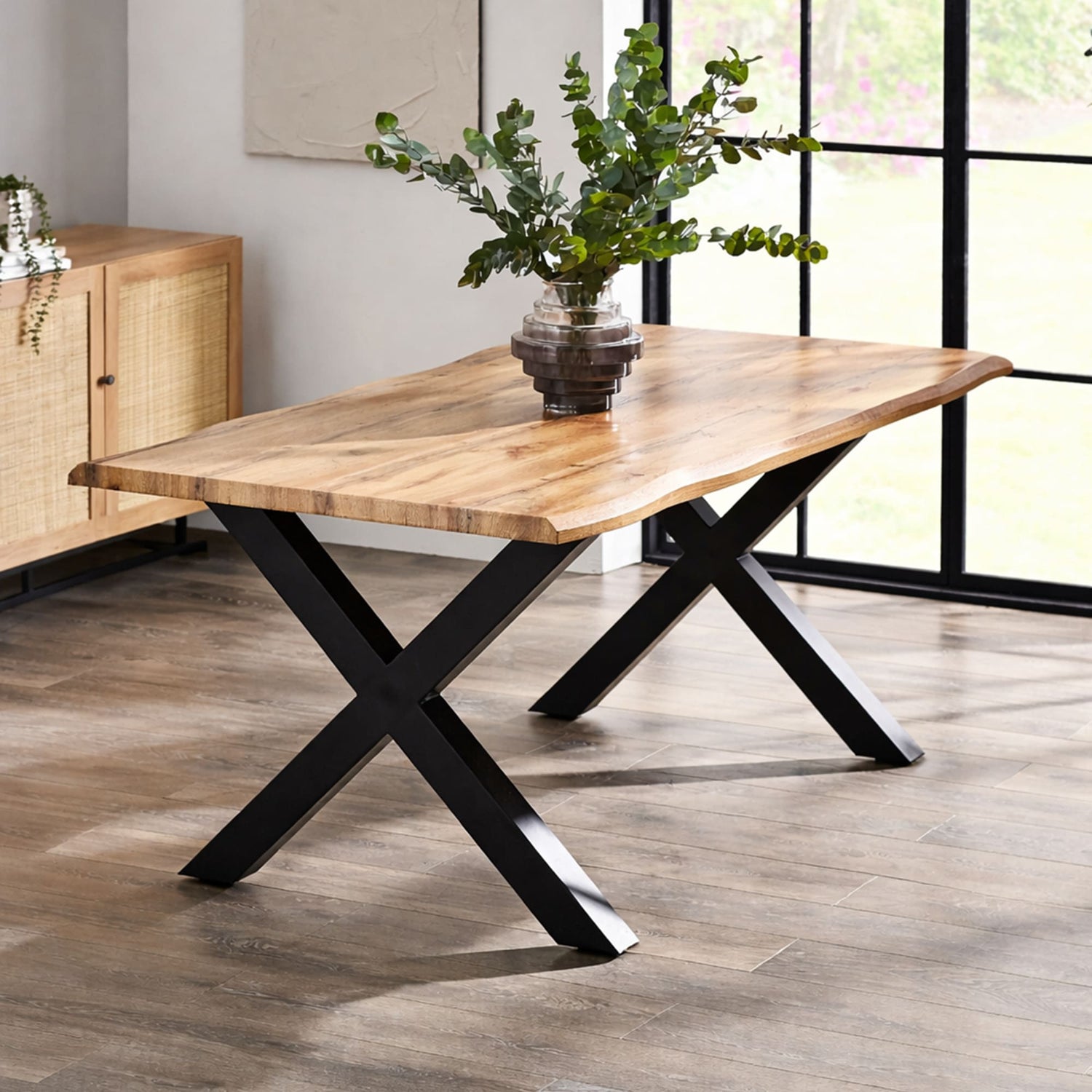 Wooden dining table with black metal legs in a room with large windows.