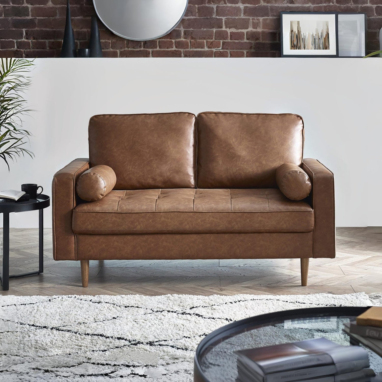 Brown leather sofa in a living room setting with a brick wall and decorative items.