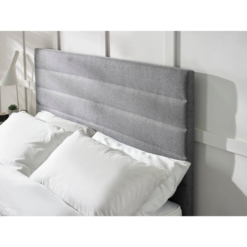 Gray upholstered headboard with white pillows against a neutral wall.