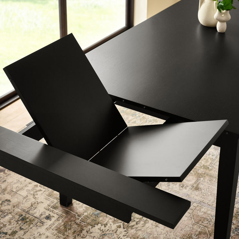 Black dining table with a chair pulled out in a room with large windows.