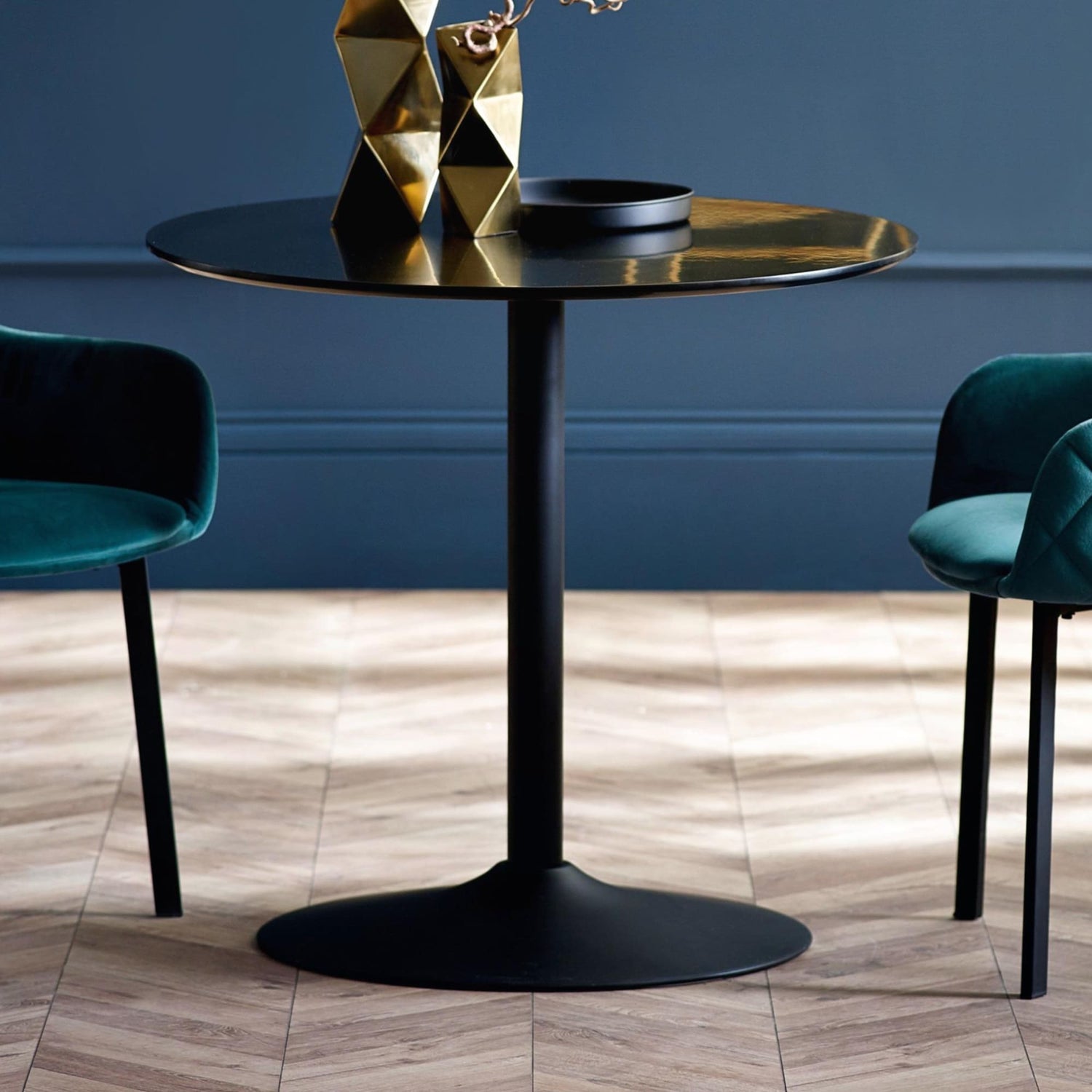Modern black round table with gold decorative items against a blue wall.