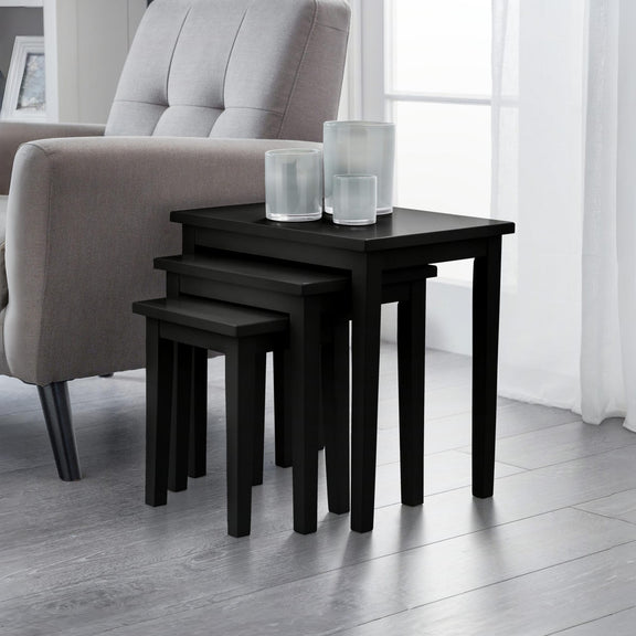 Set of black nesting tables with glass containers on a light wood floor.