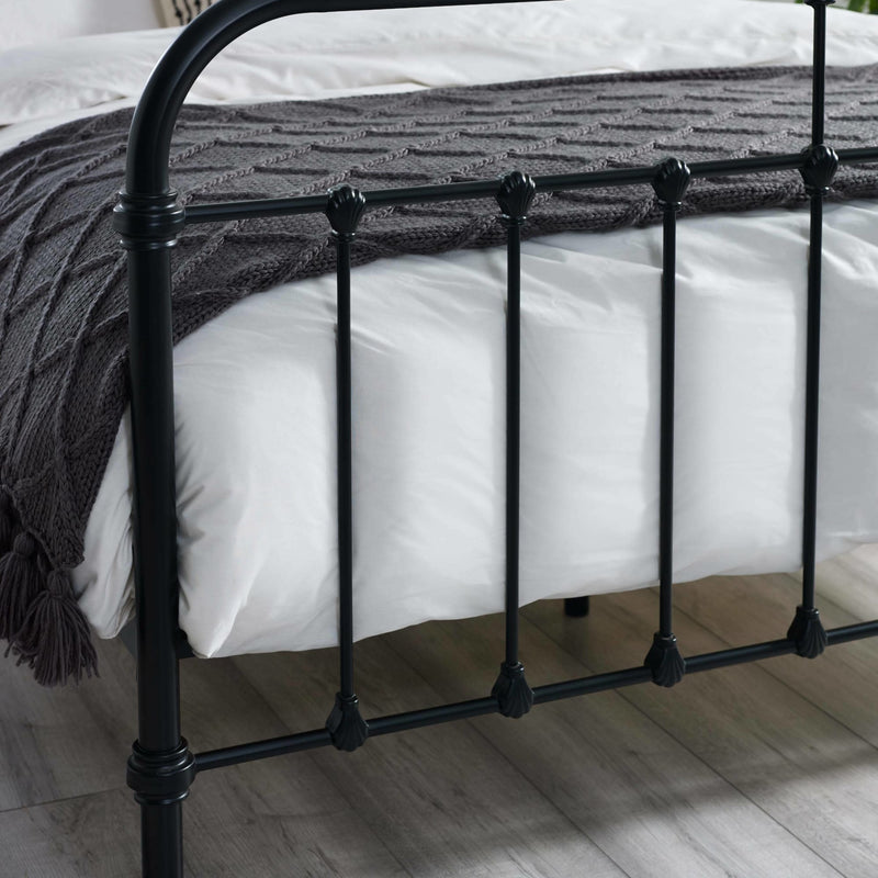 Black metal bed frame with white bedding and a dark gray blanket on a wooden floor.