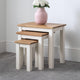 Set of three nesting tables with a pink vase and white flowers on top against a plain wall.