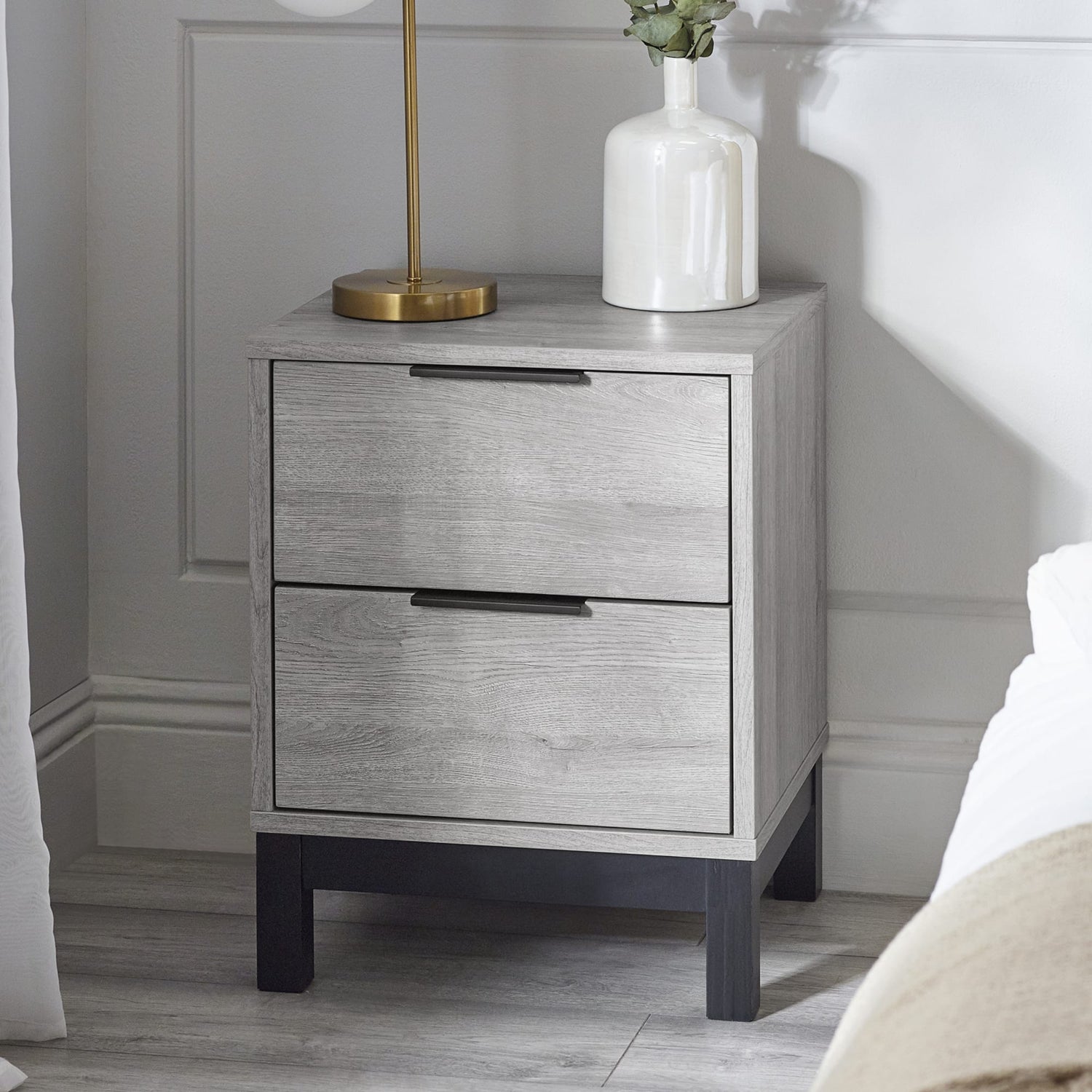Gray nightstand with two drawers, a lamp, and a vase in a bedroom setting.