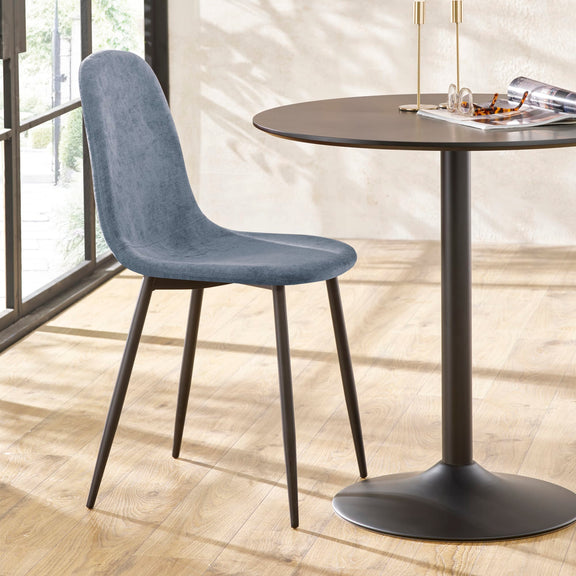 Blue chair next to a round black table on a wooden floor with a blurred background