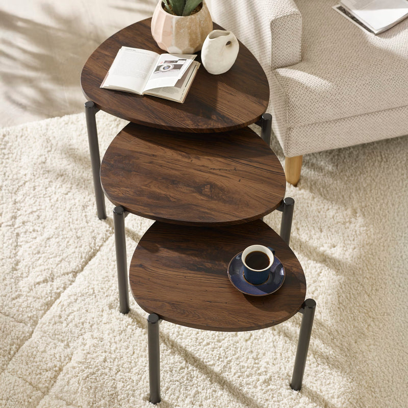 Set of three wooden side tables with a cup and saucer on a carpeted floor.