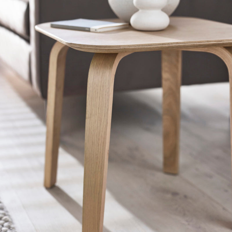 Wooden side table with a white vase and phone on a light wooden floor.