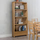 Wooden bookshelf with books and decor items against a white wall, with chairs and a table in the foreground.