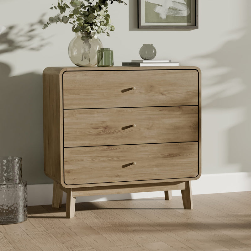 Wooden dresser with three drawers in a room with a vase of flowers and a framed picture on a shelf.