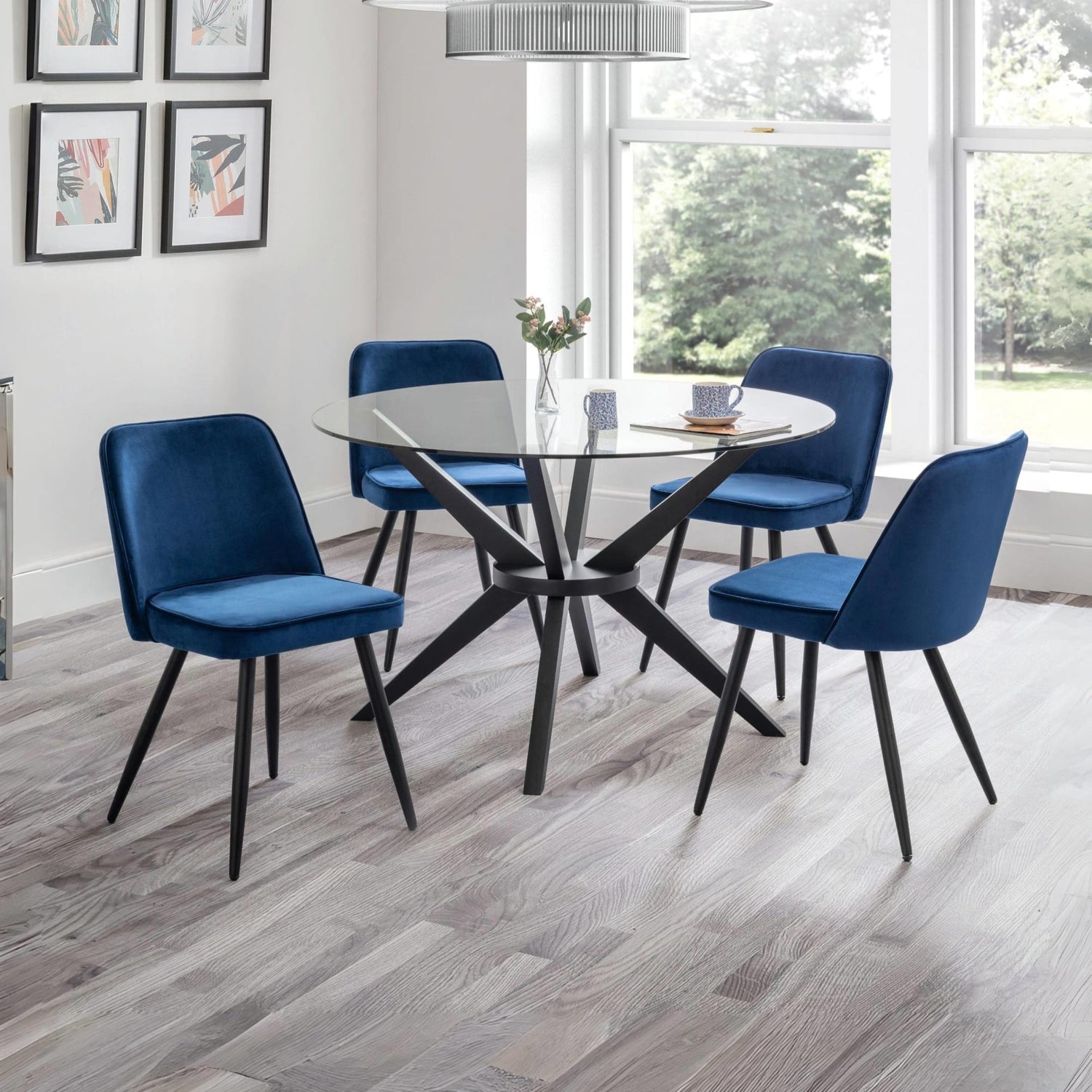 Dining room with a round glass table and four blue chairs on a wooden floor.