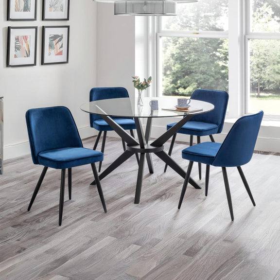 Dining room with a round glass table and four blue chairs on a wooden floor.