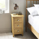 Wooden bedside table with lamp and drawers next to a bed in a bedroom.
