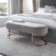Gray upholstered bench with gold legs in front of a bed in a bedroom.