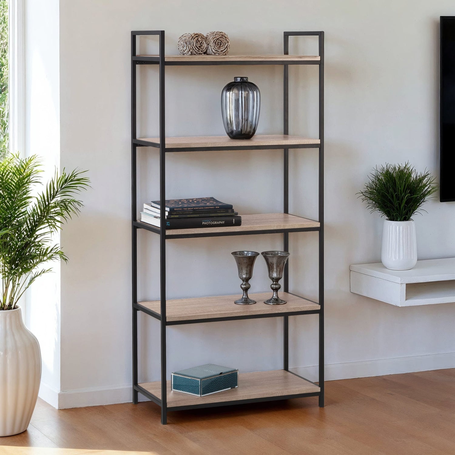 Bookshelf with decorative items in a room with plants and a window.