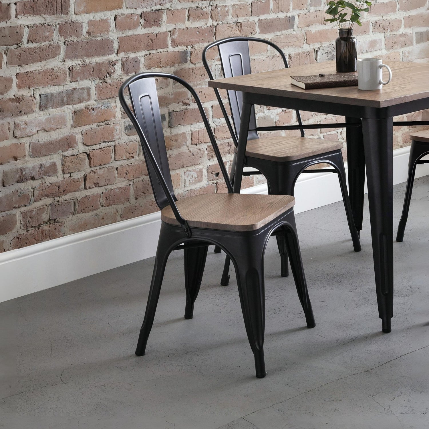 Black metal chairs with wooden seats around a wooden table against a brick wall.