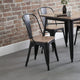 Black metal chairs with wooden seats around a wooden table against a brick wall.