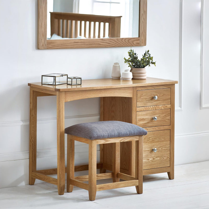Wooden dressing table with mirror, stool, and decorative items in a bright room.