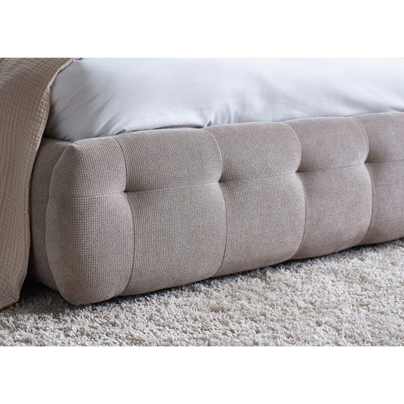 Close-up of a tufted beige headboard on a bed with white bedding.