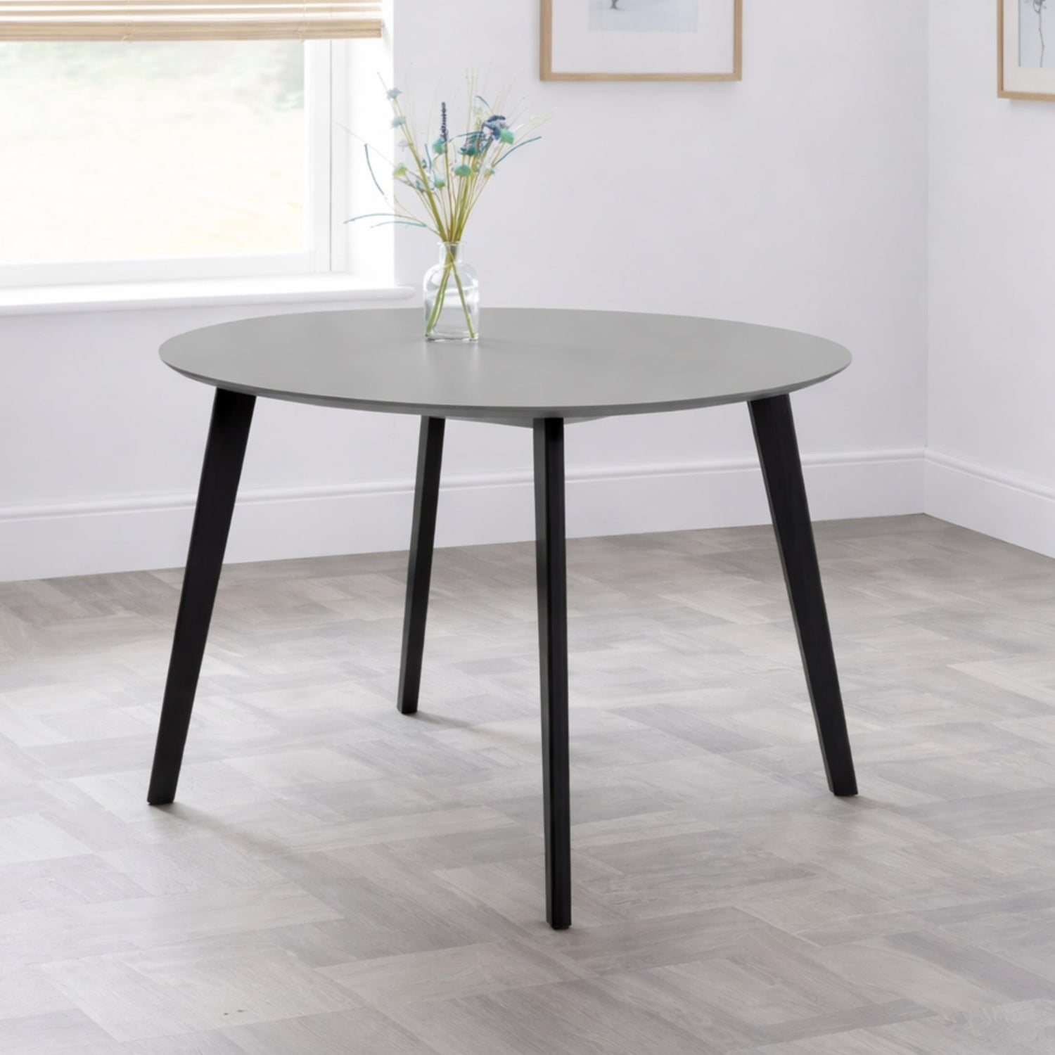 Round dining table with black legs in a room with a window and light-colored floor.