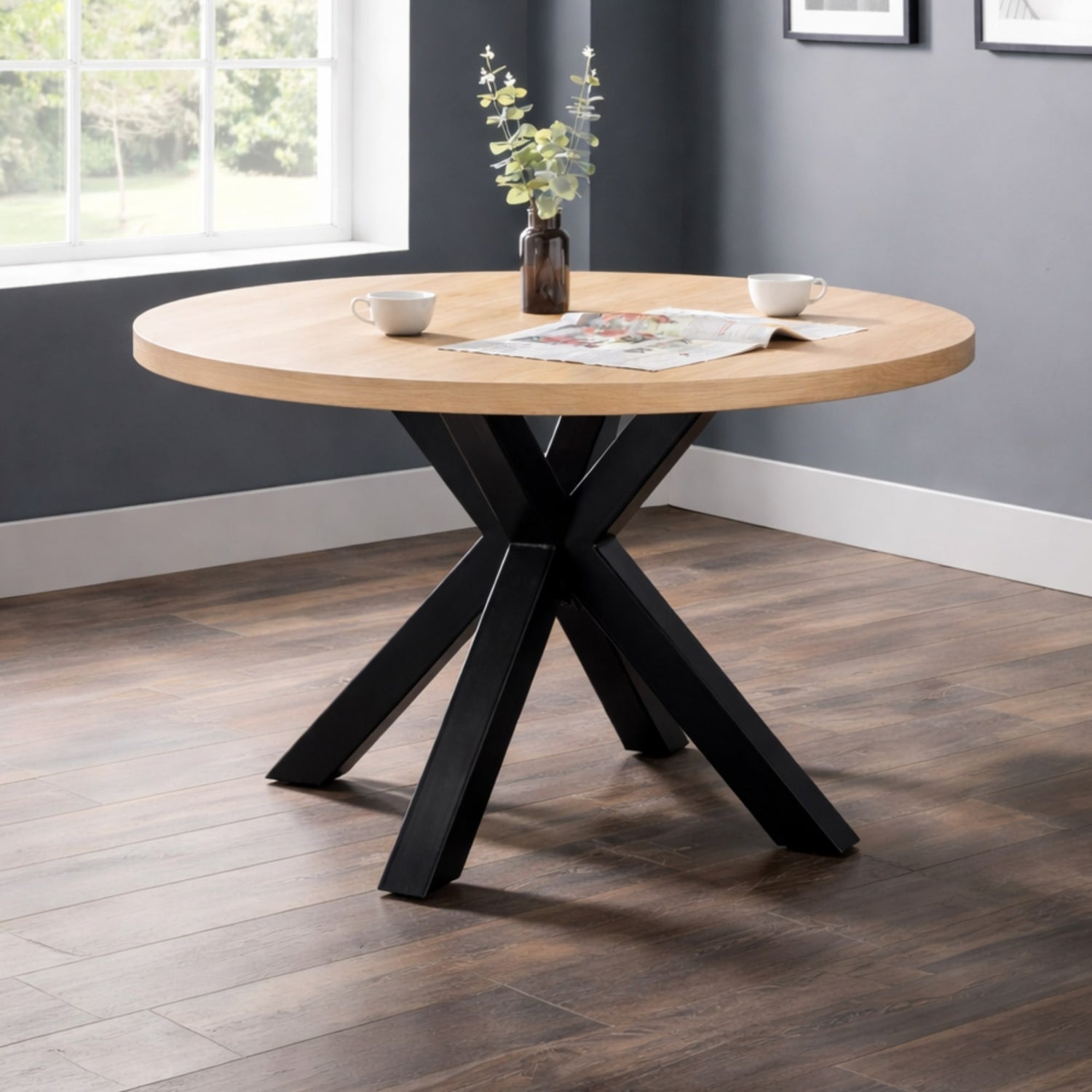 Round wooden table with black metal legs in a room with a window and gray walls.