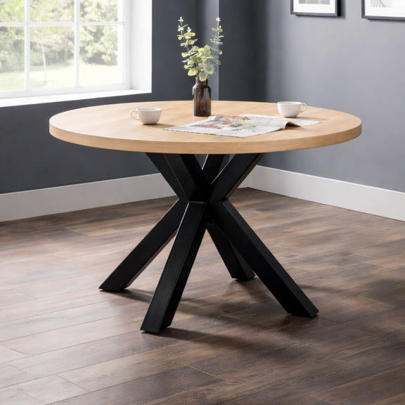 Round wooden table with black metal legs in a room with a window and gray walls.