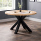 Round wooden table with black metal legs in a room with a window and gray walls.