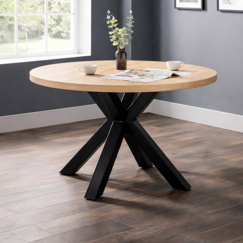 Round wooden table with black metal legs in a room with a window and gray walls.