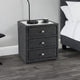 Gray textured nightstand with three drawers next to a bed in a bedroom setting.