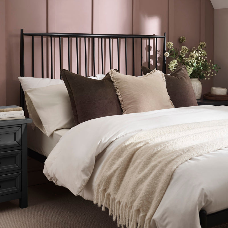 Neatly made bed with decorative pillows and a nightstand in a bedroom setting.