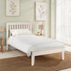 White wooden bed in a bedroom with light green walls, framed botanical art, and a lamp.