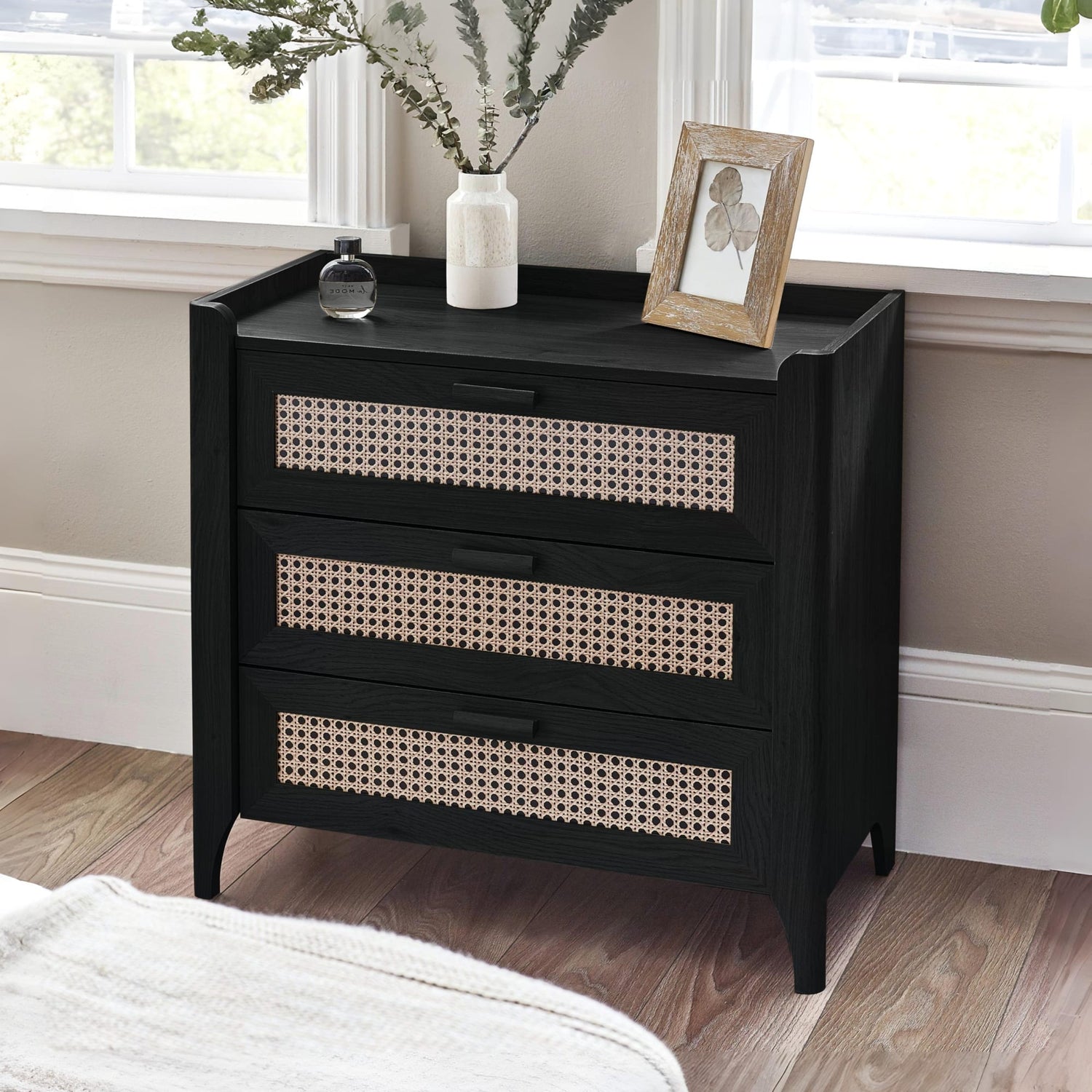 Black nightstand with wicker drawers in a bedroom setting