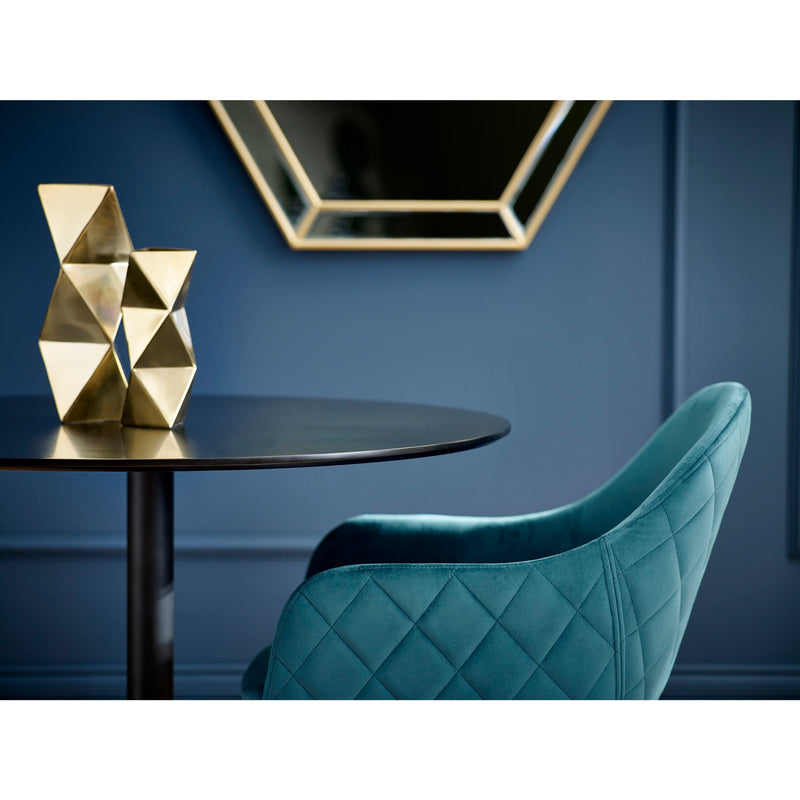 Teal chair in a room with a dark blue wall, gold geometric sculptures, and a hexagonal mirror.