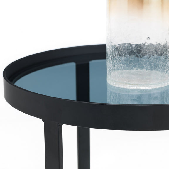 Black round side table with a glass top holding a decorative vase.
