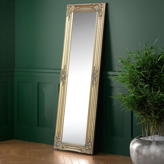 Decorative floor mirror with ornate frame against a green wall