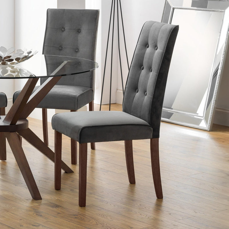 Gray upholstered chairs with wooden legs around a glass dining table.