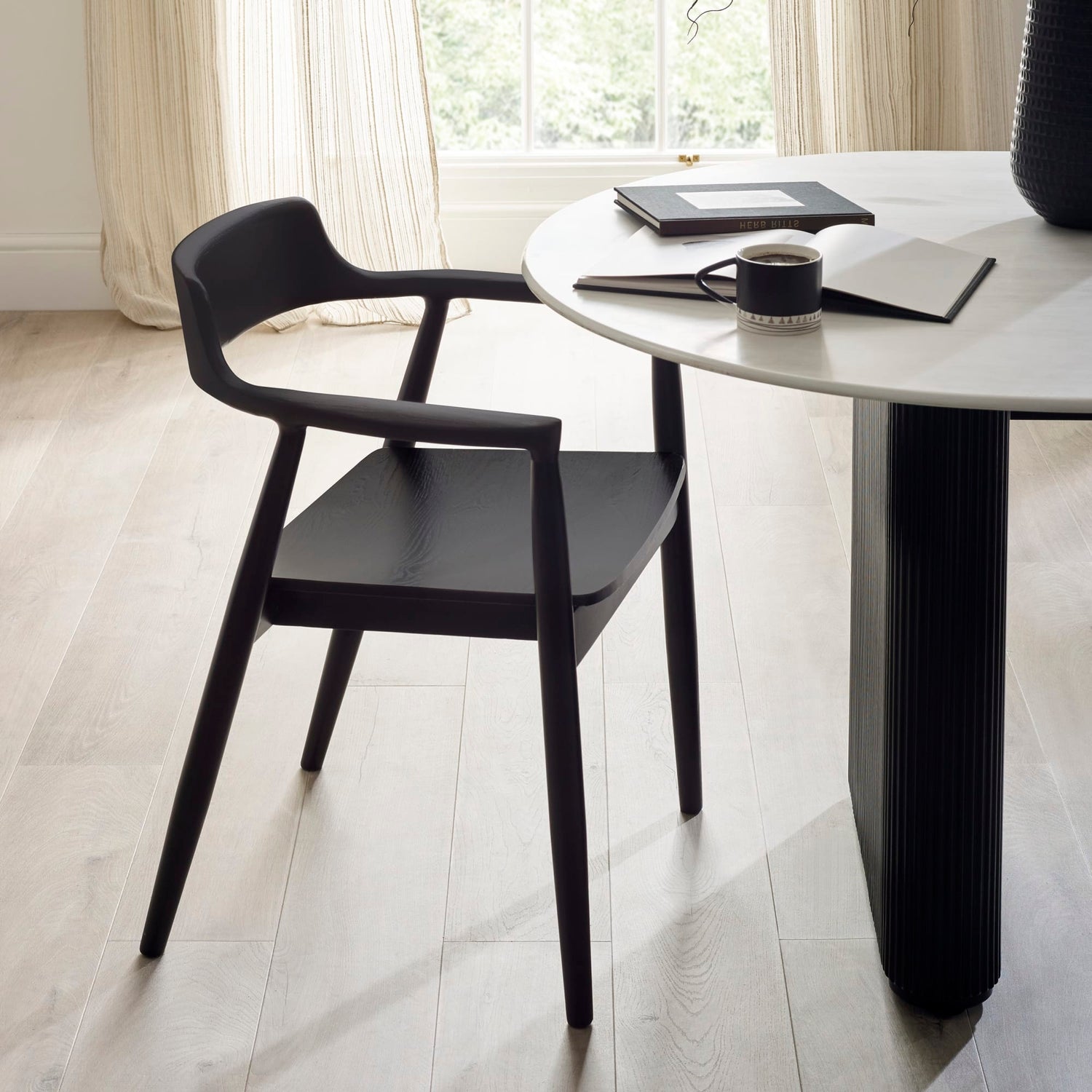 Black chair and table set in a room with light wood flooring and curtains.
