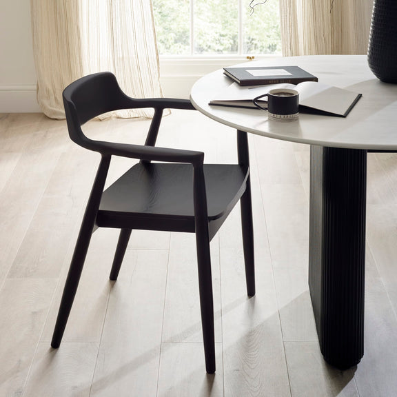 Black chair and table set in a room with light wood flooring and curtains.