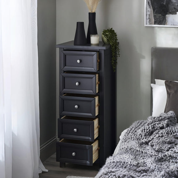 Black tall drawer unit next to a bed in a bedroom setting