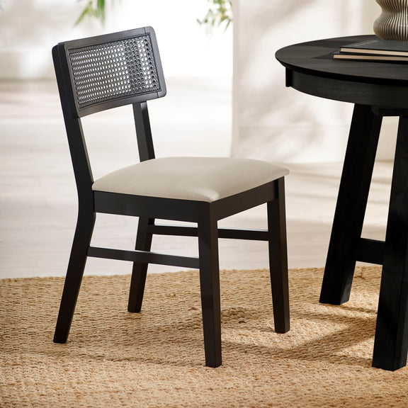 Black chair with woven backrest and white cushion next to a black round table on a beige rug.