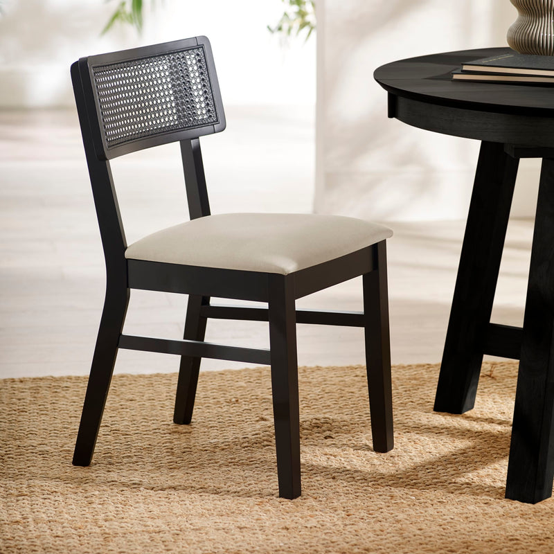 Black chair with woven backrest and white cushion next to a black round table on a beige rug.