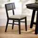 Black chair with woven backrest and white cushion next to a black round table on a beige rug.