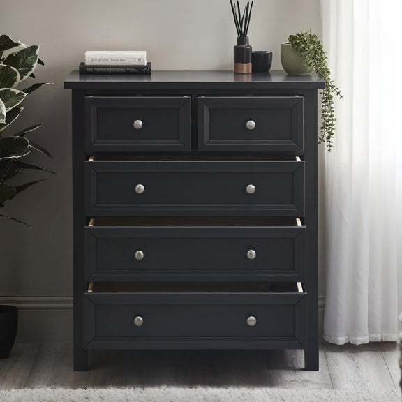 Black dresser with five drawers in a room setting with plants and books.