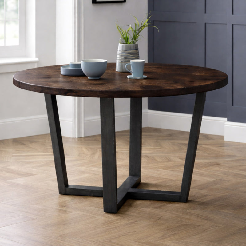Round wooden table with dark metal legs in a room with a window and wall.
